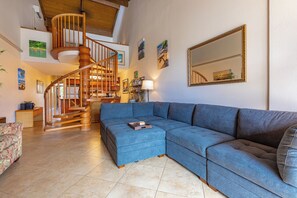 A spacious living room with a large blue sectional sofa, a wooden spiral staircase, and a large mirror on the wall.