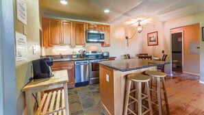 A kitchen with wooden cabinets, stainless steel appliances, a bar area with stools, and a chandelier. - Mountain Condo Near Gondola & Village 249 (Mammoth Lakes)