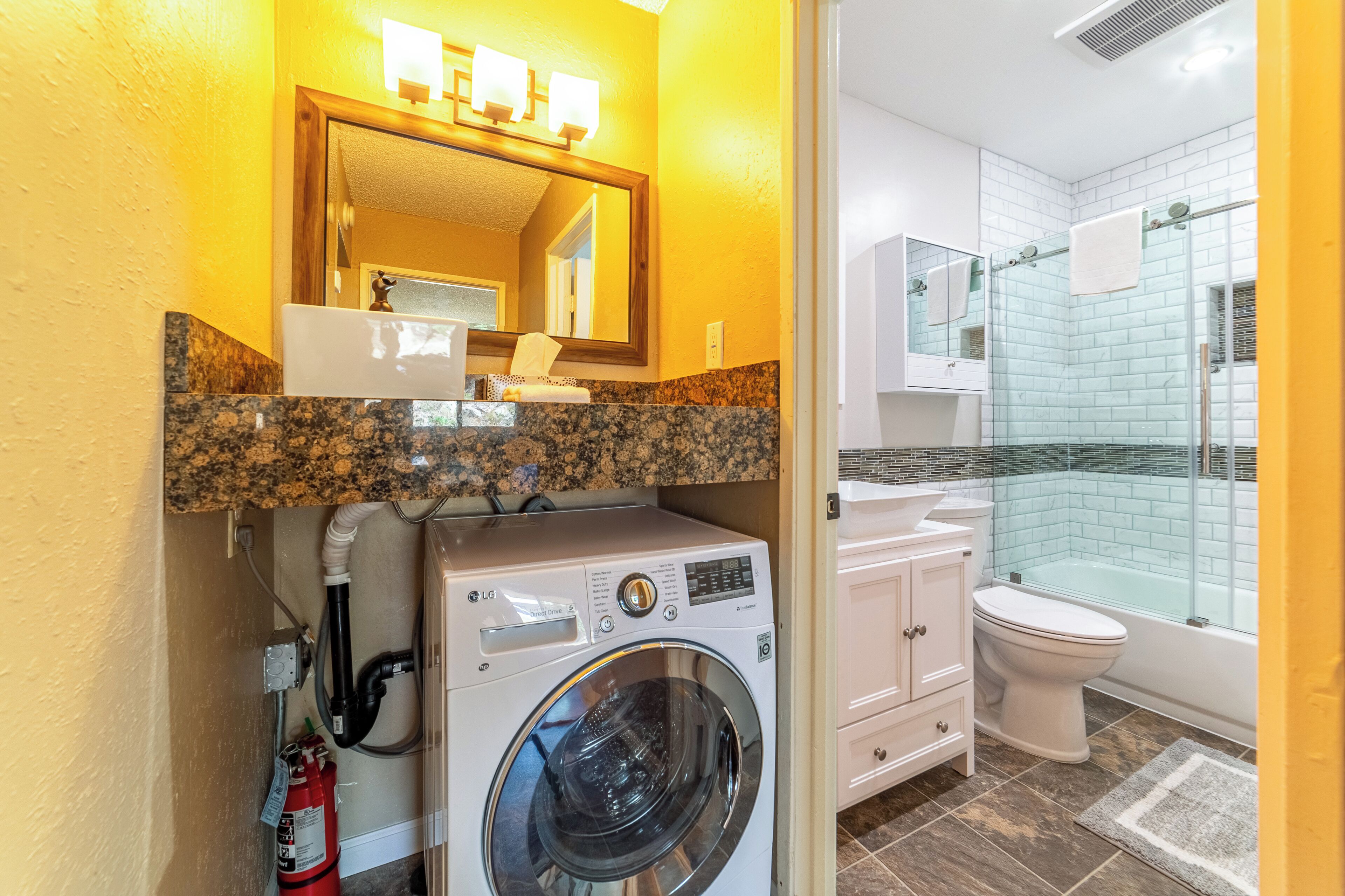 Baño compacto con lavadora, inodoro y ducha con cerramiento de vidrio.