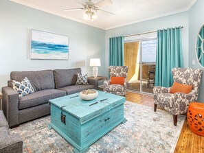 A living room with a grey sofa, patterned armchairs, a turquoise coffee table, and a view to the outside.