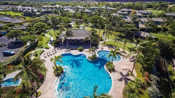An aerial view of a resort with a central swimming pool surrounded by palm trees and a mountainous backdrop. - Two-Story Private Home at Kamilo - Grill Deck, Pool & Sunset Views! (Kamuela)