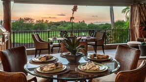 A dining area with a glass table, wicker chairs, and a view of a lush landscape during sunset. - Two-Story Private Home at Kamilo - Grill Deck, Pool & Sunset Views! (Kamuela)