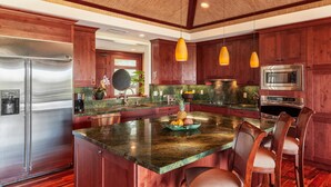 A modern kitchen with wooden cabinets, stainless steel appliances, and a large island with seating. - Two-Story Private Home at Kamilo - Grill Deck, Pool & Sunset Views! (Kamuela)