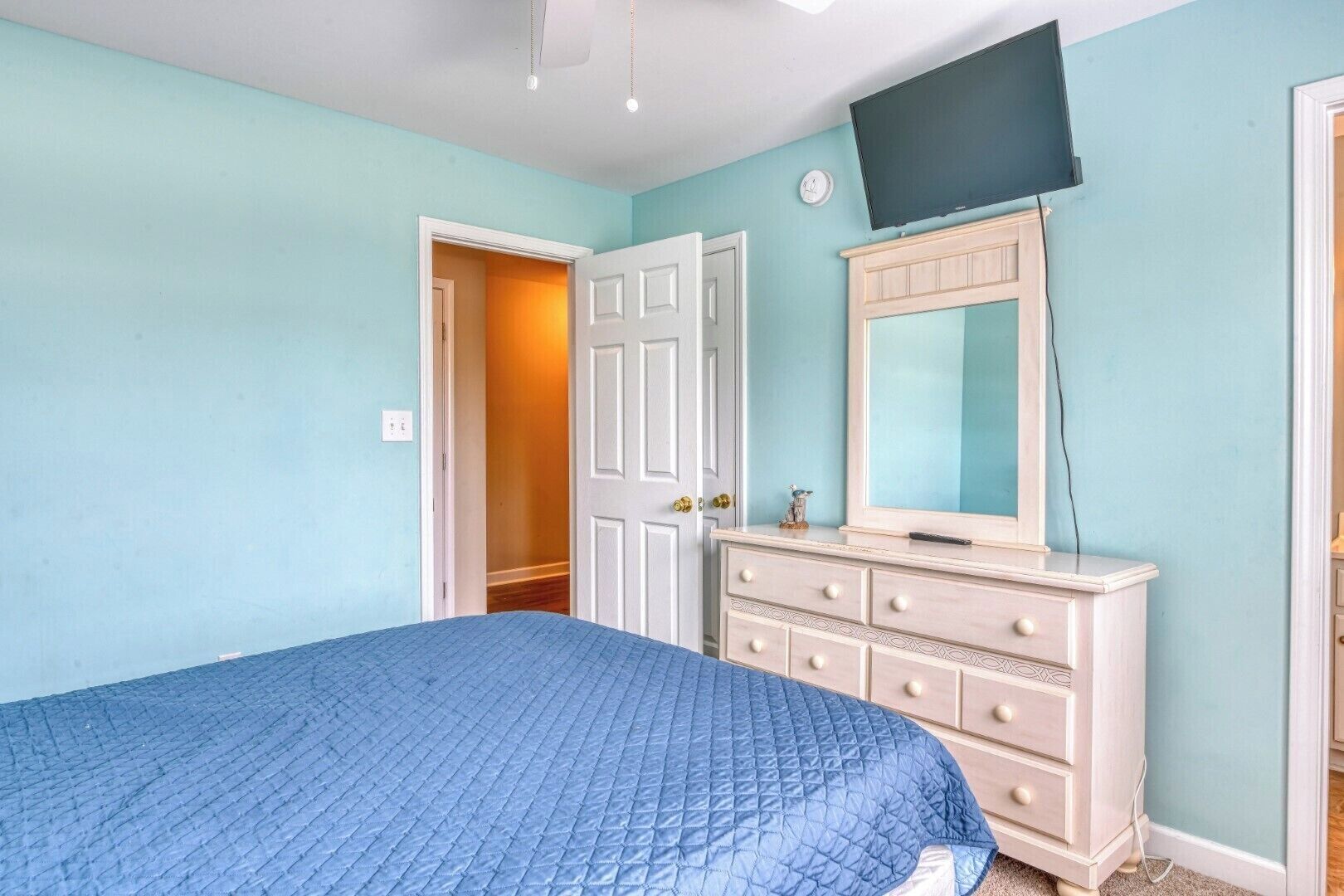 Une chambre à coucher comprenant un lit, une commode, un téléviseur et une porte donnant sur une autre pièce.