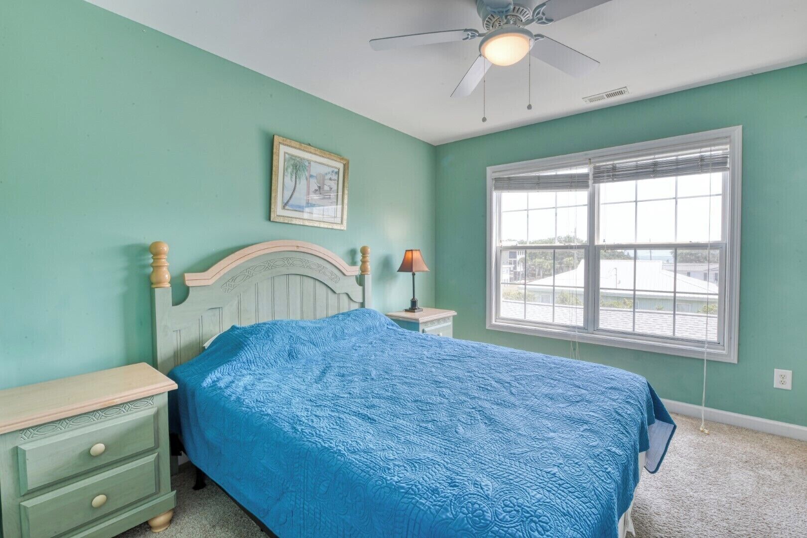 A bedroom with a bed, a nightstand, a lamp, a ceiling fan, and a window with blinds.