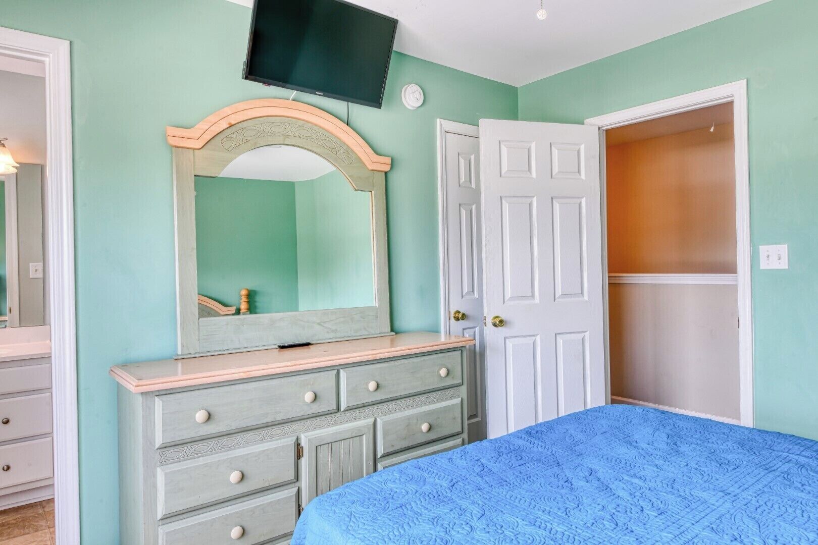 A bedroom with a bed, dresser, mirror, television, and wardrobe.