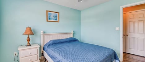 A bedroom with a bed, a nightstand, a lamp, a ceiling fan, and a door.