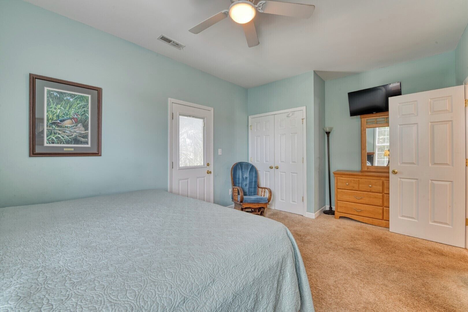 Une chambre à coucher comprenant un lit, une chaise, une commode et un ventilateur de plafond.