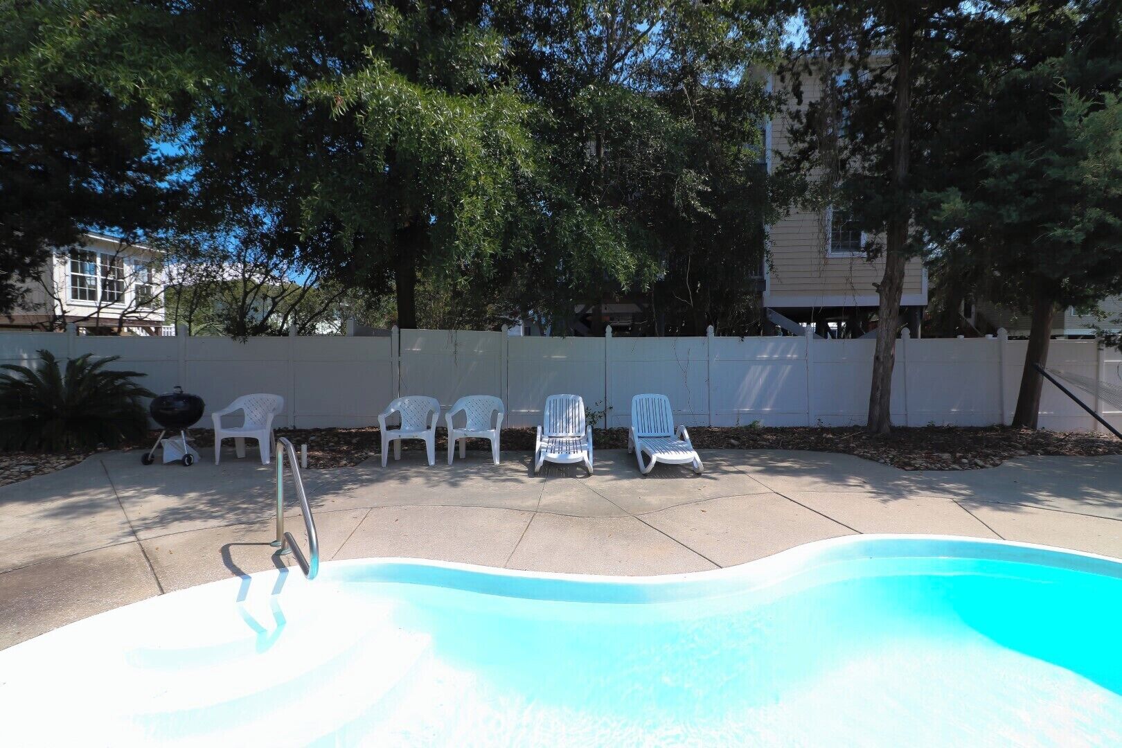 A swimming pool with lounge chairs, a barbecue grill, and a white fence.