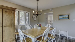 A dining room with a wooden table, white chairs, a chandelier, a clock, and a painting on the wall.