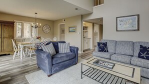 A spacious living room with a blue sofa, a white coffee table, and a dining area with a wooden table and chairs.