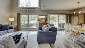 A spacious living room with a large window, a television, and a dining area with a table and chairs.