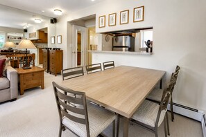A dining area with a wooden table, chairs, a sofa, and a kitchen in the background.