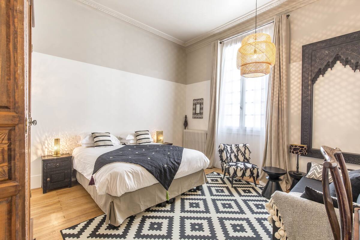 Ein Schlafzimmer mit Bett, Nachttischen, einem Sessel, einem Spiegel und einer Pendelleuchte.