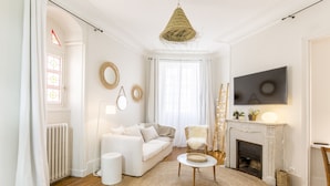 Ein Wohnzimmer mit einem weißen Sofa, einem runden Couchtisch, einem Kamin und einem an der Wand befestigten Fernseher.