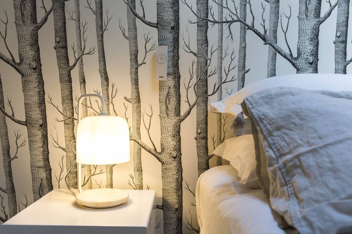 Ein Schlafzimmer mit Nachttisch, Lampe und Bett mit weißer Decke.