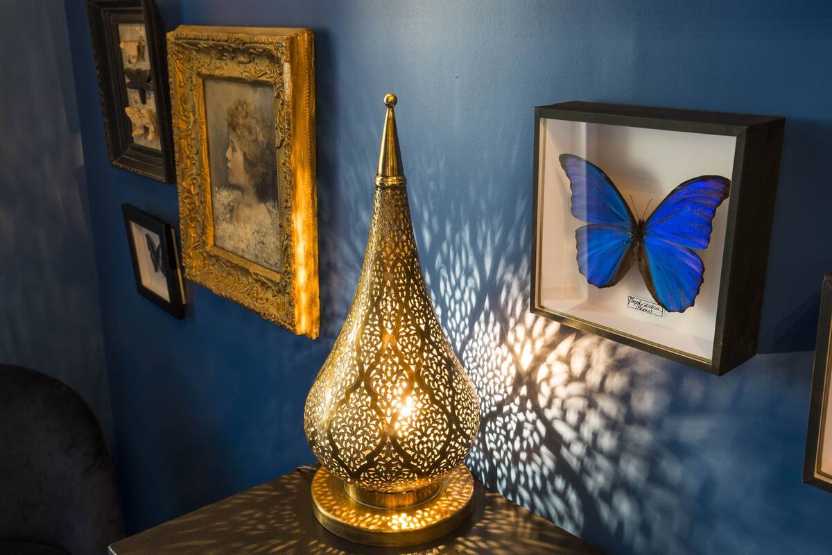 Eine dekorative Lampe mit filigranen Mustern, gerahmte Kunstwerke an der Wand und eine Schmetterlingssammlung.