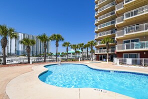 A swimming pool with a curved edge, surrounded by palm trees and a multi-story building with balconies. - Updated & beachfront w/ balcony for stunning views! 🌅 (Destin)