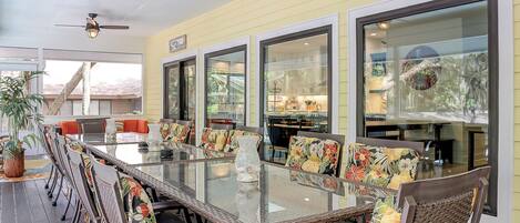 A sunlit patio with a glass-top table, wicker chairs, and a ceiling fan.