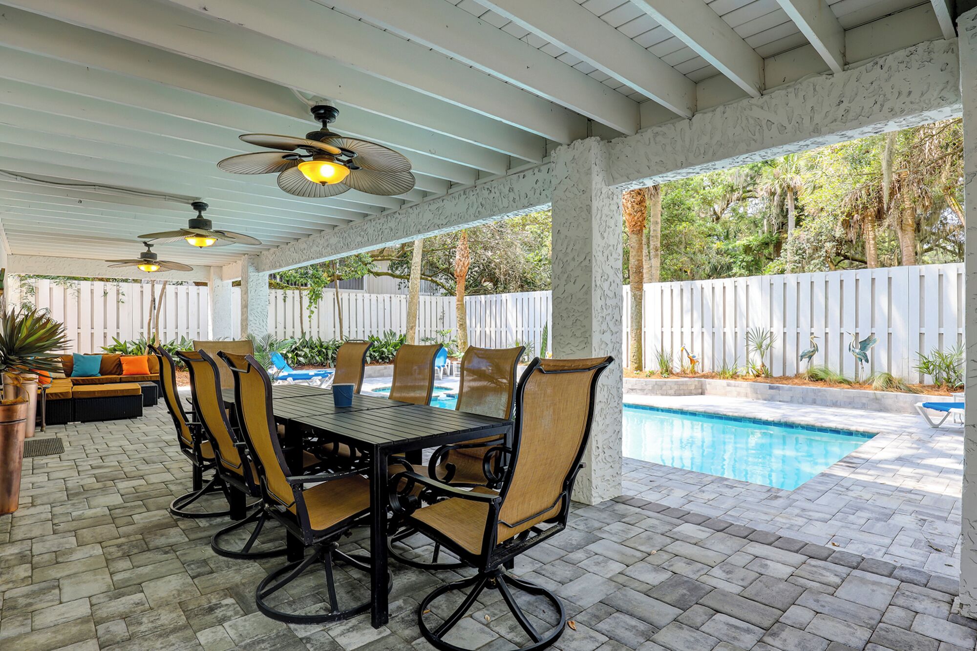 An outdoor patio with a pool, covered seating, and ceiling fans.