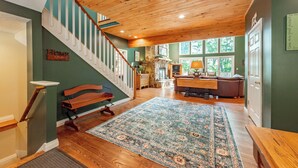 Un vaste espace de vie agrémenté d’un escalier en bois, d’un grand tapis et offrant une vue sur l’extérieur grâce à de grandes fenêtres.