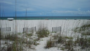 Ein Strand mit Sand, spärlicher Vegetation und wolkenlosem Himmel.