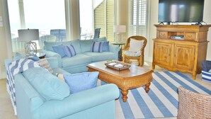 Ein Wohnzimmer mit einem hellblauen Sofa, einem Holztisch und einem Fernseher auf einer Holzkommode.
