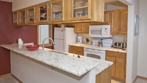A kitchen with wooden cabinets, a white countertop, a sink, a microwave, a toaster, and a refrigerator.