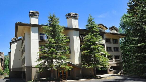 A multi-story building with a central entrance, balconies, and a parking area.