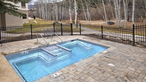 An outdoor swimming pool with a black metal fence, a hot tub, and a brick patio.