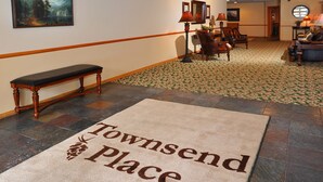 A lobby with a bench, a carpet with 'Townsend Place' text, and a painting on the wall.