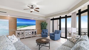 A spacious living room with a large flat-screen TV, comfortable seating, a ceiling fan, and a balcony with a view. - The Oasis At Orange Beach 1901 by Liquid Life (Orange Beach)