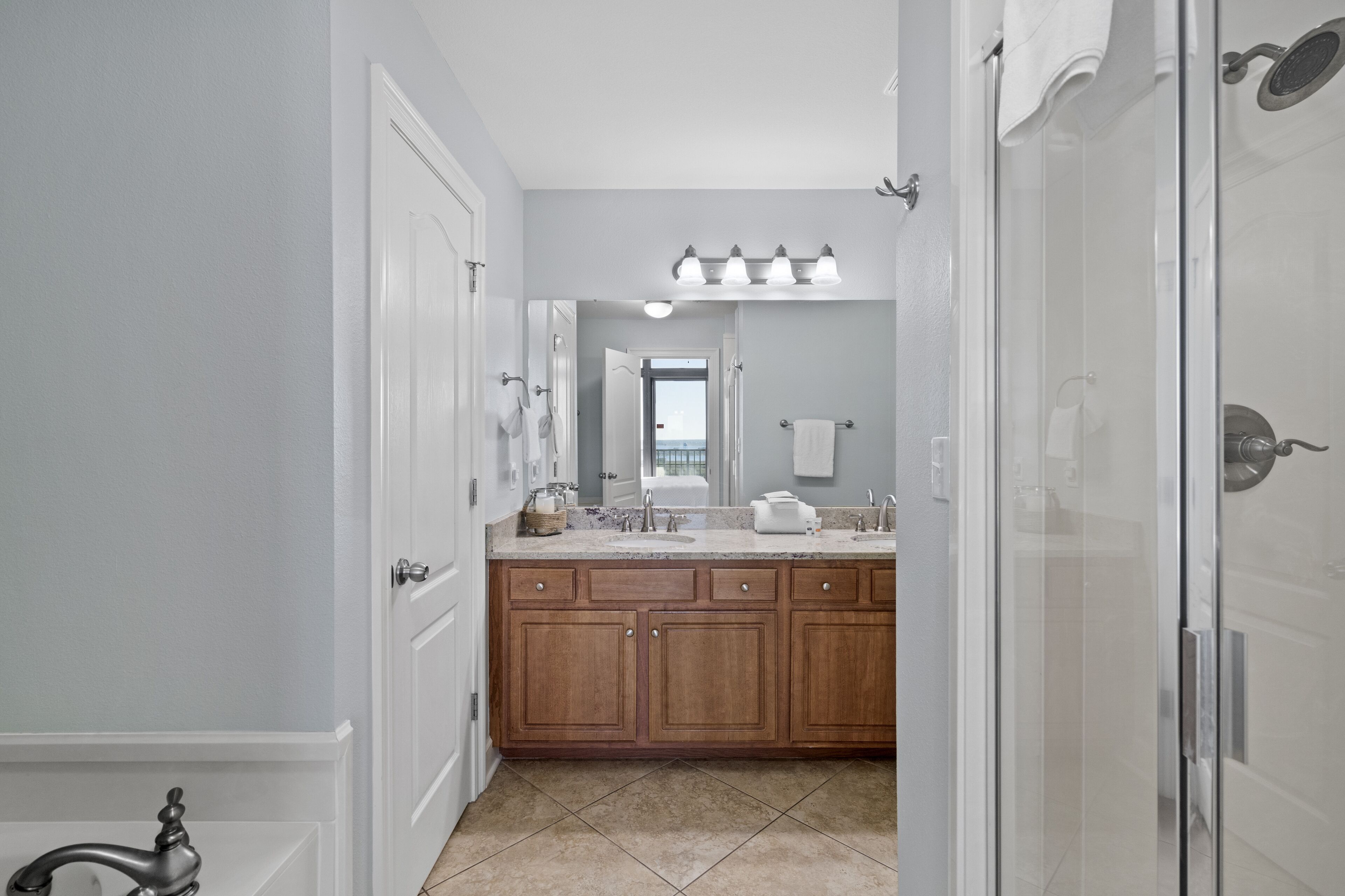 A modern bathroom with a double sink vanity, a glass shower enclosure, and a view through the door.