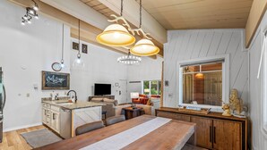 A modern kitchen with a wooden dining table, pendant lights, and a 'Welcome' sign.