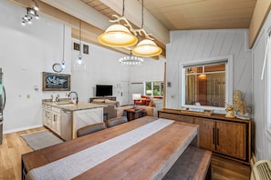 A modern kitchen with a wooden dining table, pendant lights, and a 'Welcome' sign.