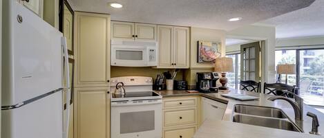 A kitchen with white appliances, a microwave, a stove, and a sink.