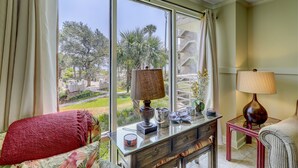 A room with a large window, a sofa, a table with decorative items, and a lamp.