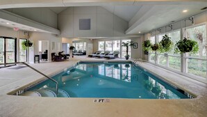 An indoor swimming pool with a 3 FT depth marker, lounge area with seating, and large windows with plants.