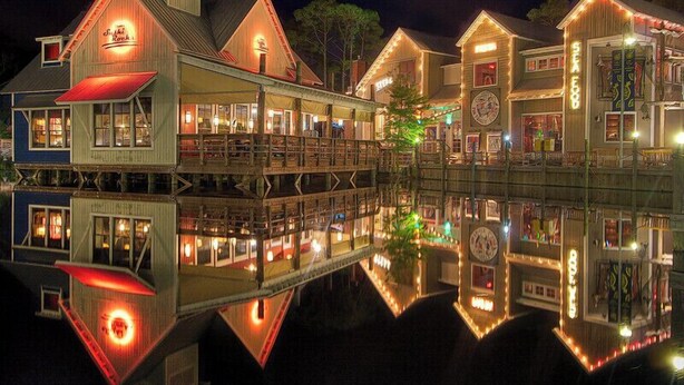 A waterfront building with multiple levels, including a docked boat, and a reflection in the water.