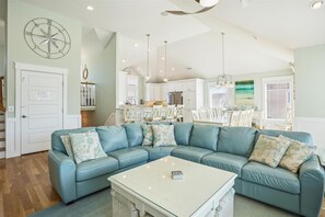 A living room with a blue sectional sofa, a white coffee table, and a kitchen in the background.