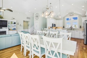 A spacious kitchen with white cabinetry, a dining area with white chairs, and a living area with a blue sofa.
