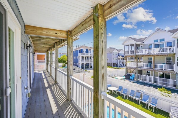 A wooden balcony with a view of a residential area, including multi-story buildings and a swimming pool.