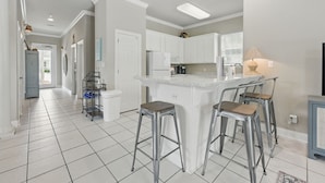 Una cocina moderna con armarios blancos, una isla central con taburetes y un refrigerador a la vista.