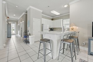 A modern kitchen with white cabinets, a central island with stools, and a visible refrigerator. - Vacation Starts Poolside–Heated Private Pool & Golf Cart Available (Santa Rosa Beach)