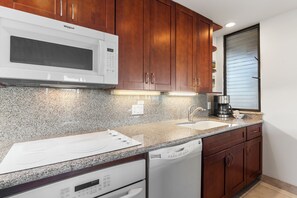 A modern kitchen with a built-in microwave, granite countertop, stainless steel sink, and wooden cabinets.