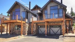 Una casa moderna de dos pisos con fachada de piedra, ventanas amplias y una terraza de madera.