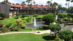 A hotel with multiple red-roofed buildings, a well-maintained lawn, a central water feature, and a variety of tropical plants.