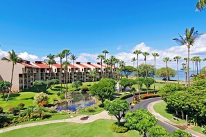 A hotel with multiple floors, a landscaped garden with a pond, palm trees, and a view of the ocean.