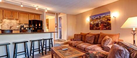 A cozy living room with a sofa, a coffee table, and a kitchen area with wooden cabinets and a refrigerator.
