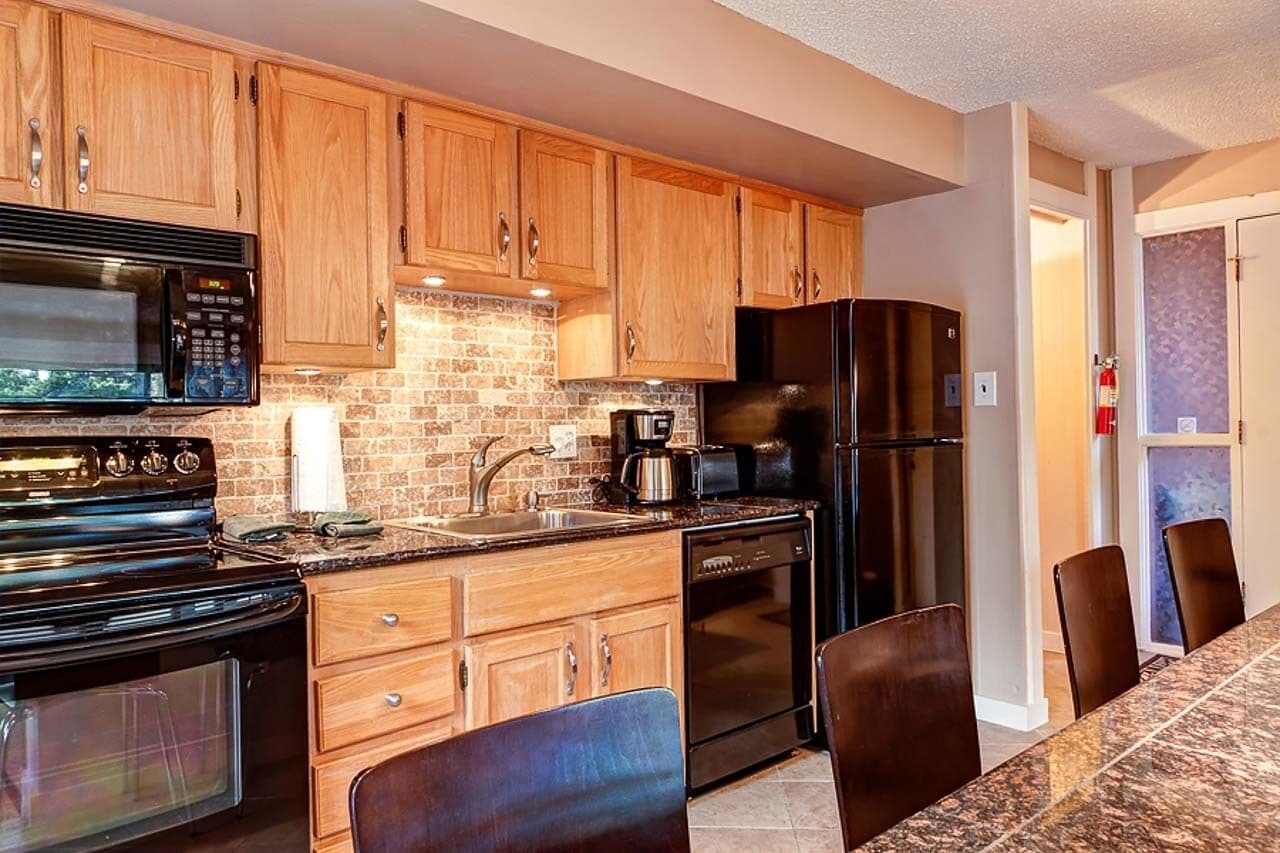 Una cocina con gabinetes de madera, estufa negra, microondas, refrigerador y cafetera.
